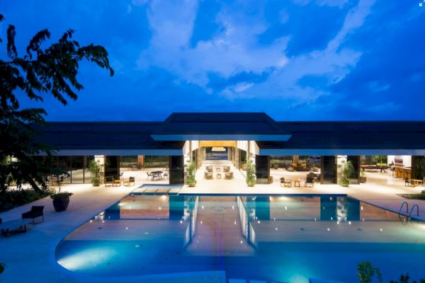 A luxurious resort at dusk, featuring an expansive swimming pool with ambient lighting, surrounded by elegant seating areas and modern architecture.