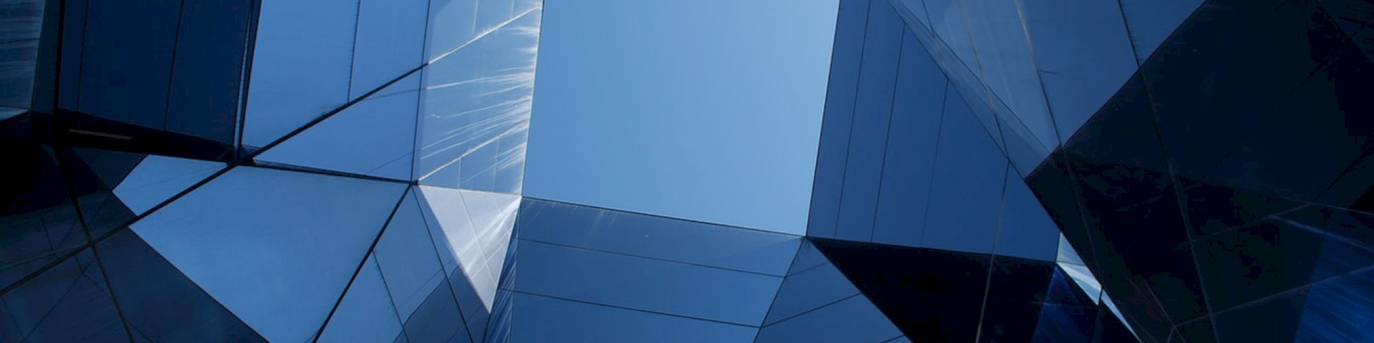 The image shows a geometric architectural structure with reflective glass panels framing a view of the sky, creating a complex and abstract visual.