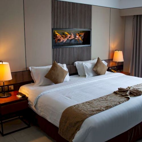 This image depicts a modern hotel room with a large bed, two bedside tables with lamps, and a decorative piece above the bed.