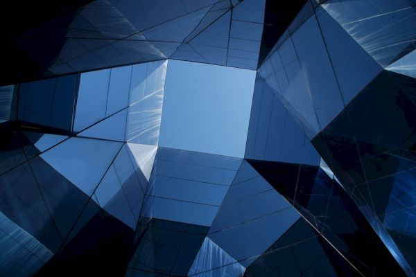 The image displays a perspective view of modern, reflective glass buildings forming an abstract geometric pattern against the sky.