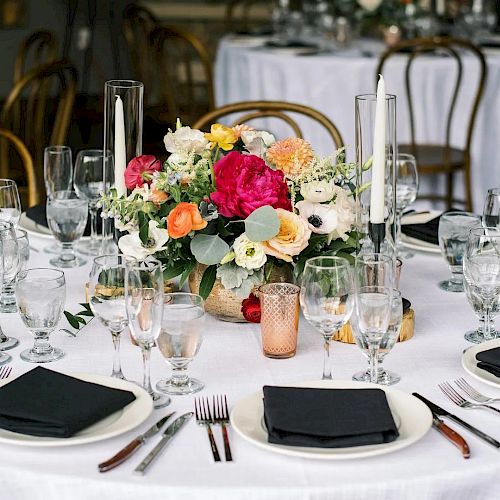 A decorated table set for an event, featuring a floral centerpiece, black napkins, glassware, and utensils on a white tablecloth.
