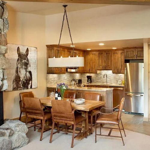 A cozy kitchen and dining area with wooden cabinets, a dining table with leather chairs, stone fireplace, and a horse painting on the wall.