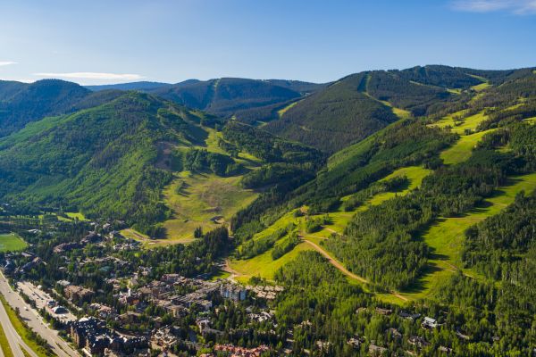 This image shows a scenic aerial view of a mountainous landscape with lush green hills, forests, and a small town nestled in a valley.