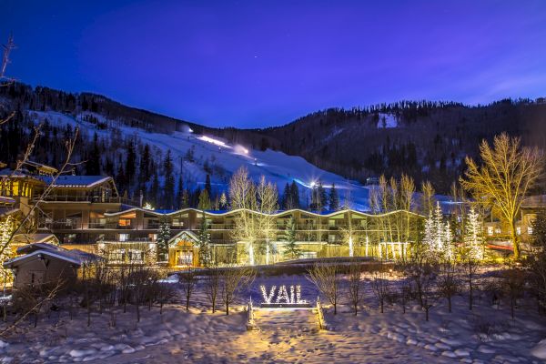 A snowy mountain resort at night with illuminated buildings and a sign that reads 