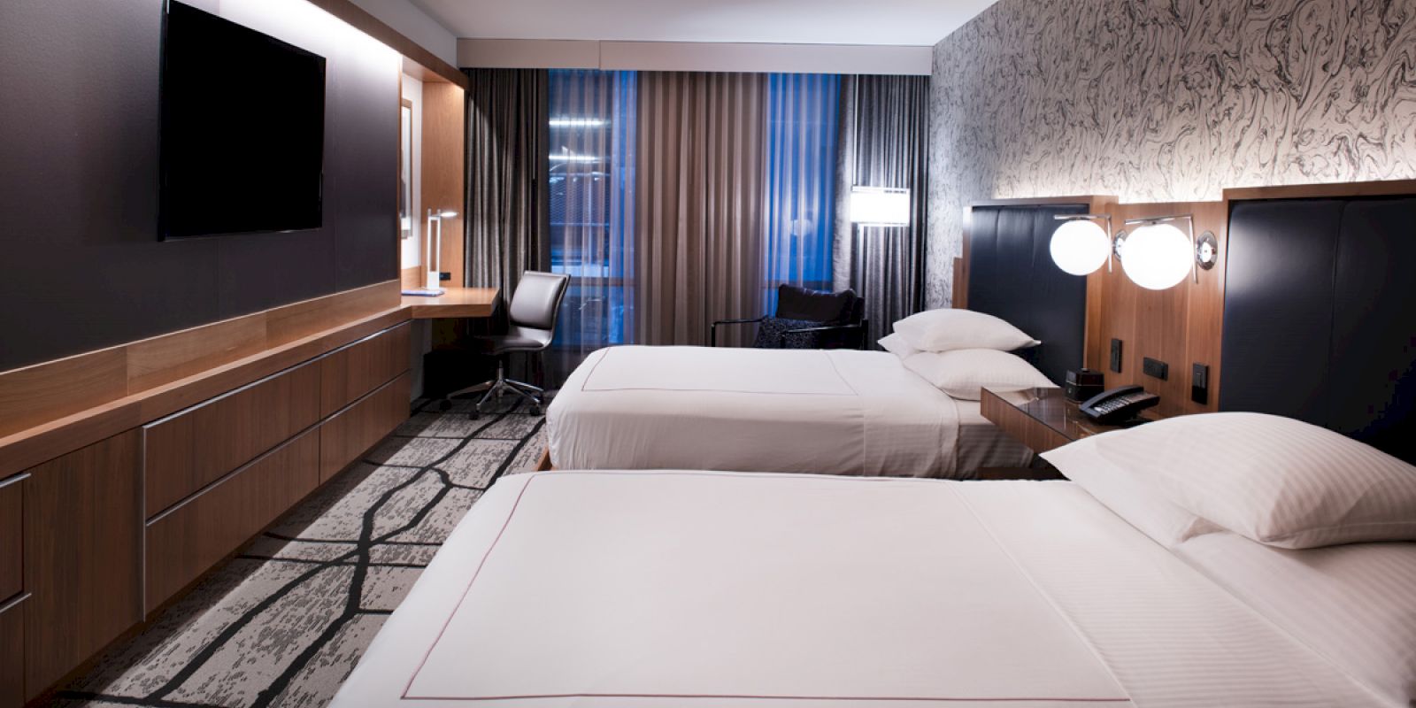 The image shows a modern hotel room with two neatly made beds, a flat-screen TV, a work desk with a chair, and stylish decor ending the sentence.
