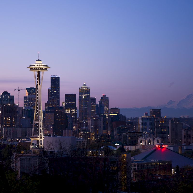 This image shows the Seattle skyline at dusk, with the Space Needle prominently featured, and Mount Rainier visible in the background.