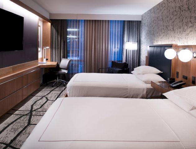 A modern hotel room with two neatly made double beds, a wall-mounted TV, a desk with a chair, and contemporary decor ending the sentence.