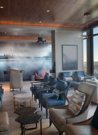 A modern lounge area with comfortable seating, ambient lighting, and a panoramic window offering a scenic view of a waterfront and ferris wheel.