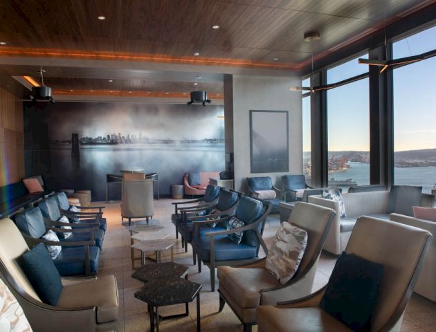 A modern lounge area with comfortable seating, ambient lighting, and a panoramic window offering a scenic view of a waterfront and ferris wheel.