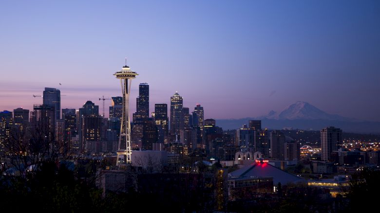 This image shows the Seattle skyline featuring the Space Needle at dusk, with Mount Rainier visible in the background against a purple and blue sky.